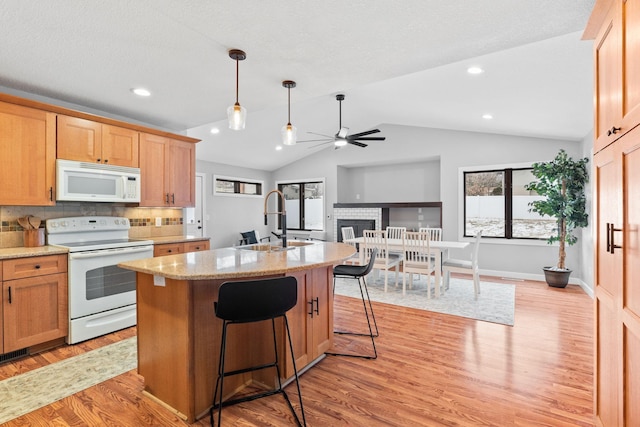 kitchen with tasteful backsplash, sink, a breakfast bar area, white appliances, and light hardwood / wood-style flooring