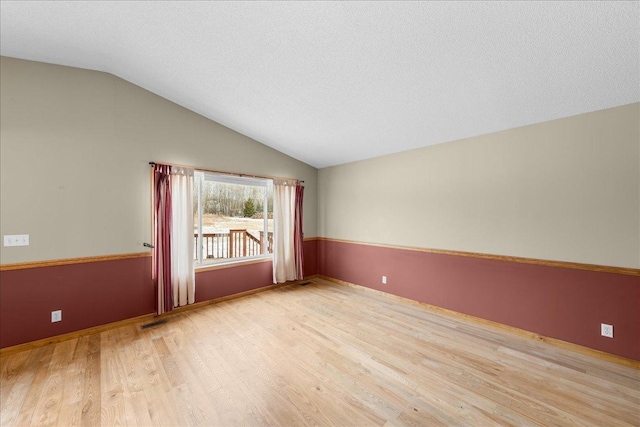 empty room featuring vaulted ceiling, a textured ceiling, and light wood-type flooring