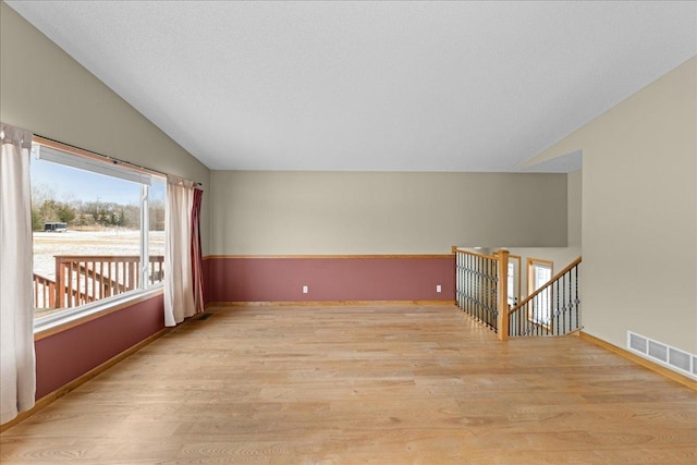 unfurnished room featuring lofted ceiling, light hardwood / wood-style floors, and a textured ceiling