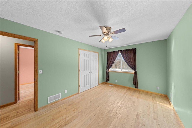 unfurnished bedroom with ceiling fan, a textured ceiling, light hardwood / wood-style floors, and a closet