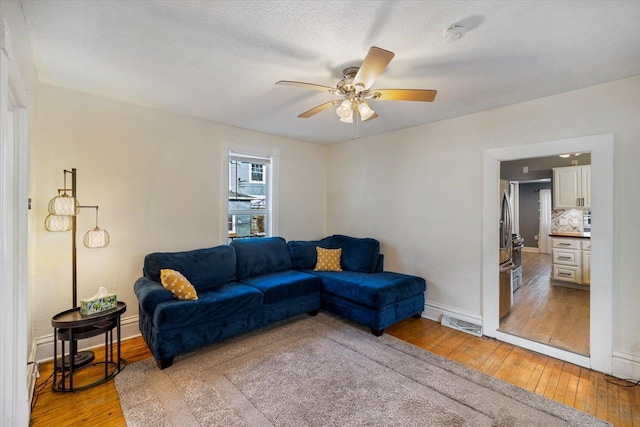 living room with ceiling fan, a textured ceiling, and light hardwood / wood-style floors