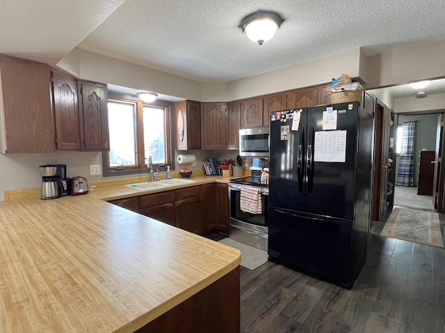 kitchen with a peninsula, dark wood-style flooring, a sink, stainless steel appliances, and light countertops