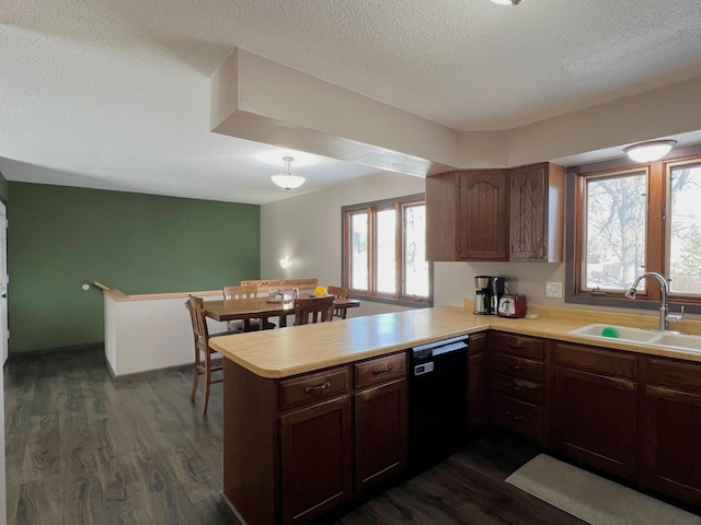 kitchen with a sink, a peninsula, light countertops, dishwasher, and dark wood-style flooring