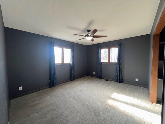 carpeted spare room with baseboards, visible vents, a wealth of natural light, and ceiling fan