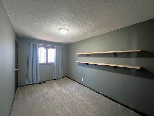 spare room with light carpet, visible vents, a textured ceiling, and baseboards