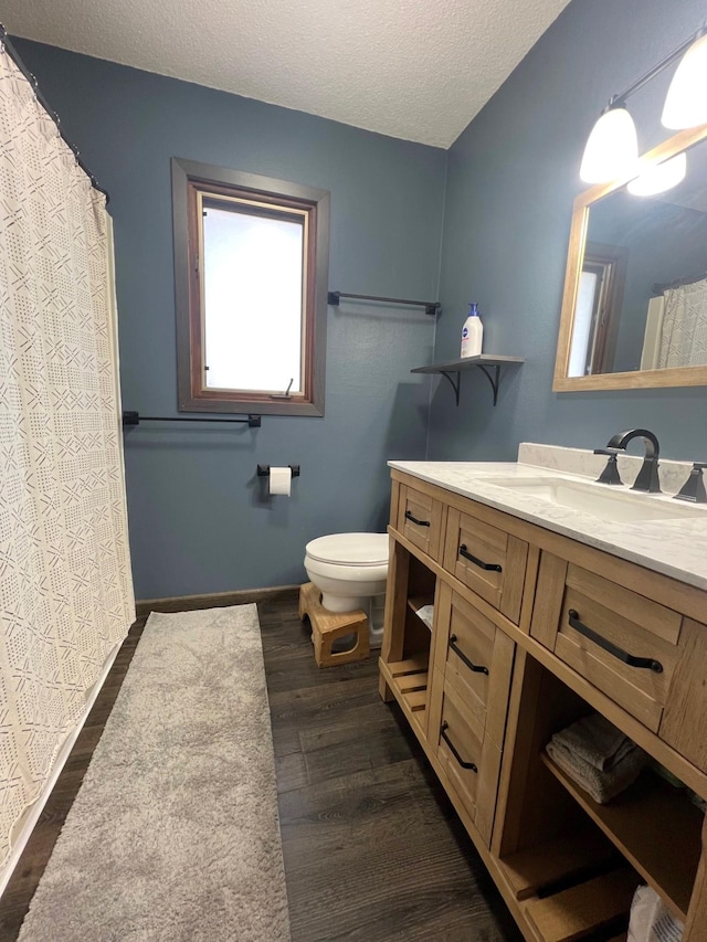 bathroom featuring baseboards, toilet, vanity, wood finished floors, and a textured ceiling