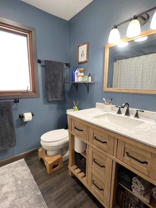 bathroom featuring toilet, a textured ceiling, wood finished floors, baseboards, and vanity