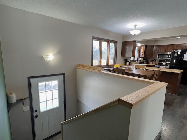 kitchen featuring a textured ceiling, dark wood finished floors, stainless steel appliances, a peninsula, and light countertops