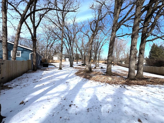 yard layered in snow featuring a detached garage and fence