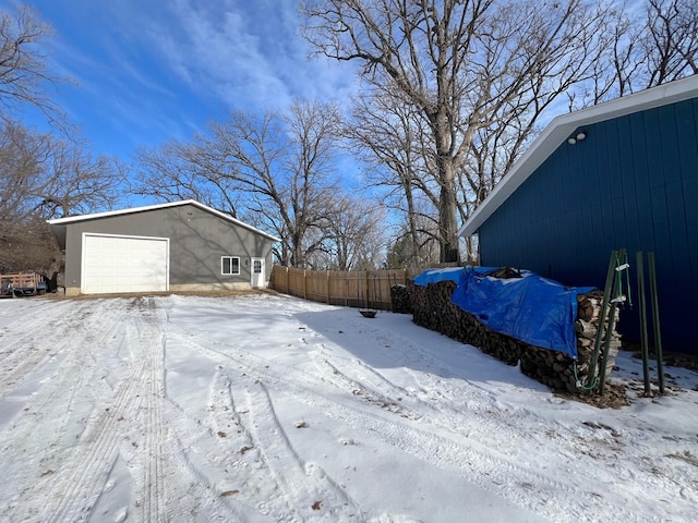 yard layered in snow featuring a detached garage, an outdoor structure, and fence