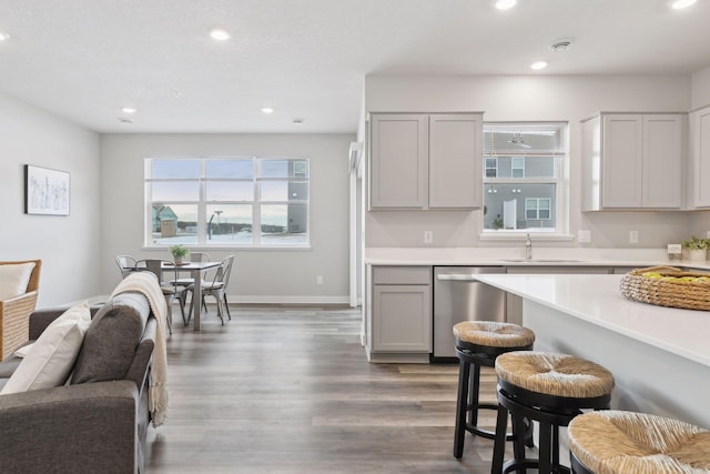 kitchen featuring sink, gray cabinetry, wood-type flooring, a kitchen bar, and stainless steel dishwasher