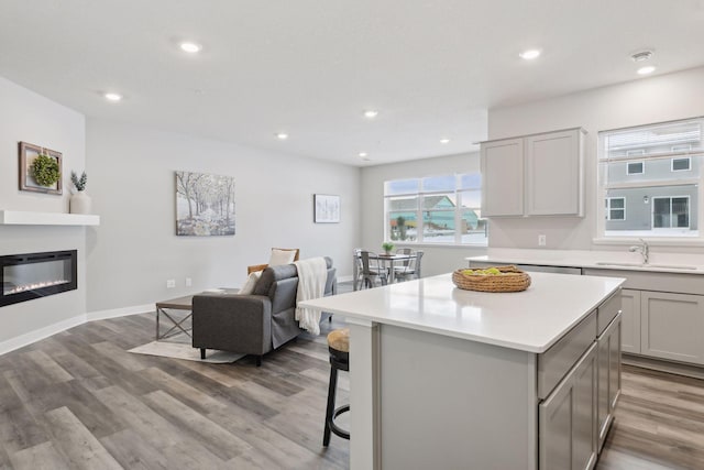 kitchen with sink, gray cabinetry, a center island, a kitchen bar, and light wood-type flooring