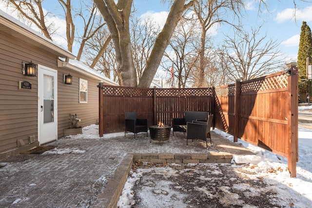 snow covered patio with an outdoor fire pit and a fenced backyard