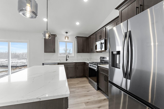 kitchen with sink, appliances with stainless steel finishes, light stone counters, light hardwood / wood-style floors, and decorative light fixtures