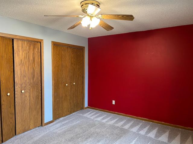 unfurnished bedroom with ceiling fan, light colored carpet, a textured ceiling, and two closets