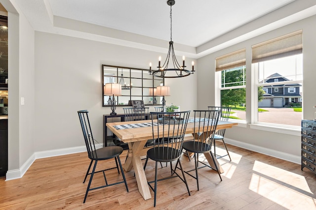 dining space with light hardwood / wood-style flooring, a notable chandelier, and a tray ceiling