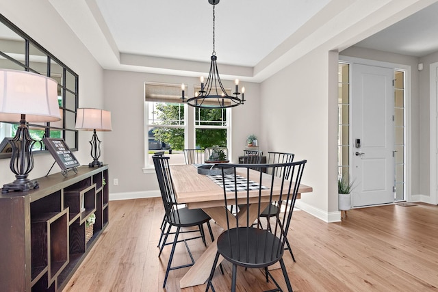 dining area with a raised ceiling, light hardwood / wood-style floors, and a notable chandelier