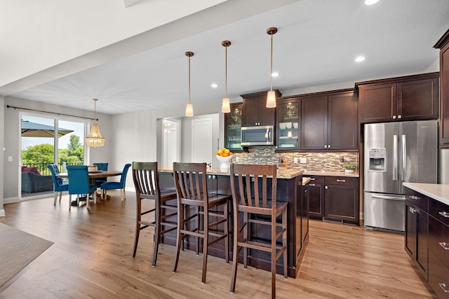 kitchen featuring tasteful backsplash, a center island, dark brown cabinets, hanging light fixtures, and appliances with stainless steel finishes