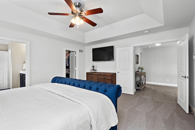 carpeted bedroom featuring ceiling fan, ensuite bathroom, a tray ceiling, and a spacious closet