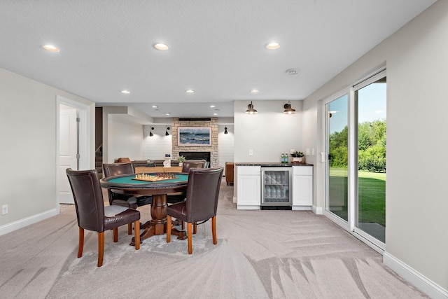 carpeted dining area featuring a stone fireplace, beverage cooler, and indoor bar