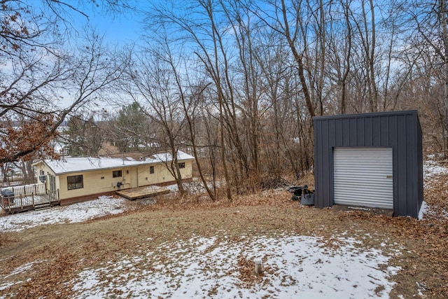 yard covered in snow with a garage, an outdoor structure, and a deck