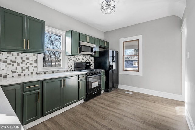 kitchen featuring decorative backsplash, black appliances, light hardwood / wood-style floors, and green cabinetry