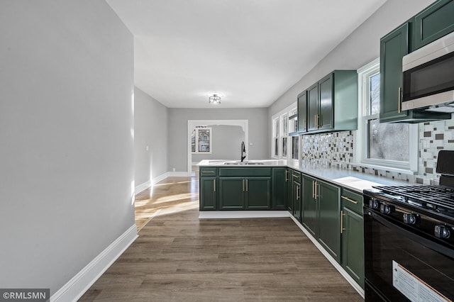 kitchen with sink, gas stove, kitchen peninsula, green cabinets, and backsplash