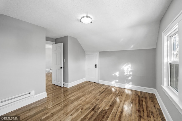 additional living space with a baseboard radiator, vaulted ceiling, hardwood / wood-style floors, and a textured ceiling