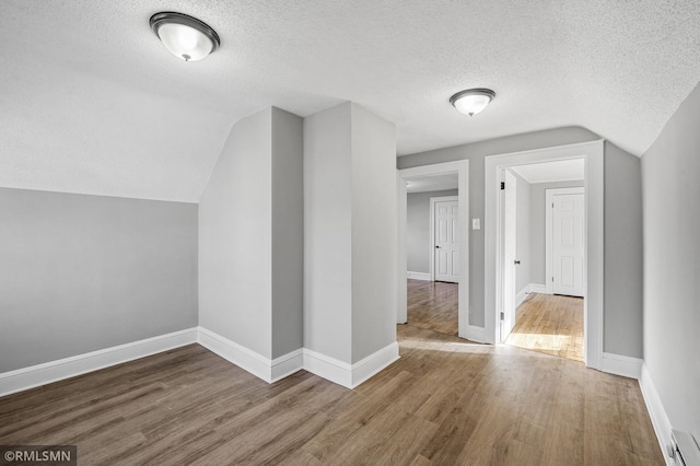 additional living space with lofted ceiling, hardwood / wood-style floors, and a textured ceiling