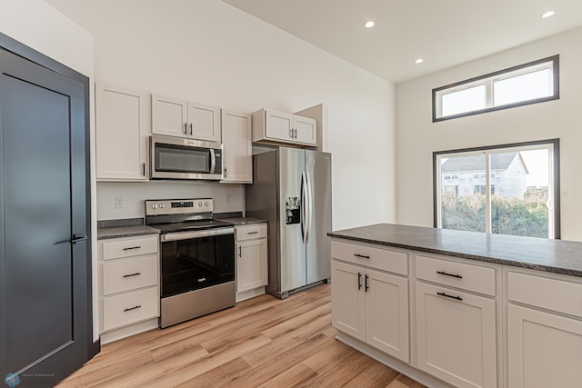 kitchen featuring white cabinetry, stainless steel appliances, light hardwood / wood-style floors, and dark stone countertops