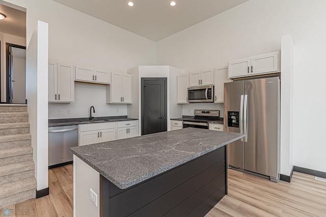 kitchen with white cabinetry, a center island, light wood-type flooring, dark stone counters, and stainless steel appliances