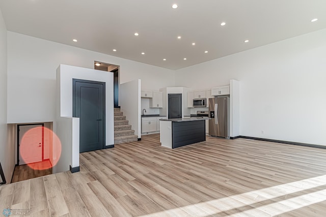 kitchen with light wood-type flooring, stainless steel appliances, white cabinets, and a kitchen island