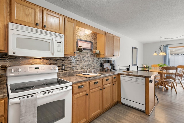 kitchen featuring tasteful backsplash, hanging light fixtures, light hardwood / wood-style flooring, kitchen peninsula, and white appliances