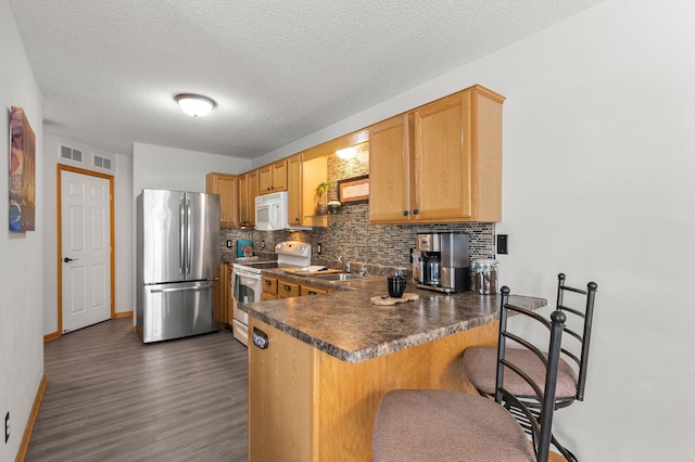 kitchen featuring white appliances, dark hardwood / wood-style floors, kitchen peninsula, and backsplash