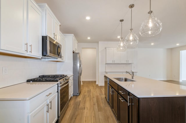 kitchen with dark brown cabinetry, sink, white cabinetry, stainless steel appliances, and a kitchen island with sink