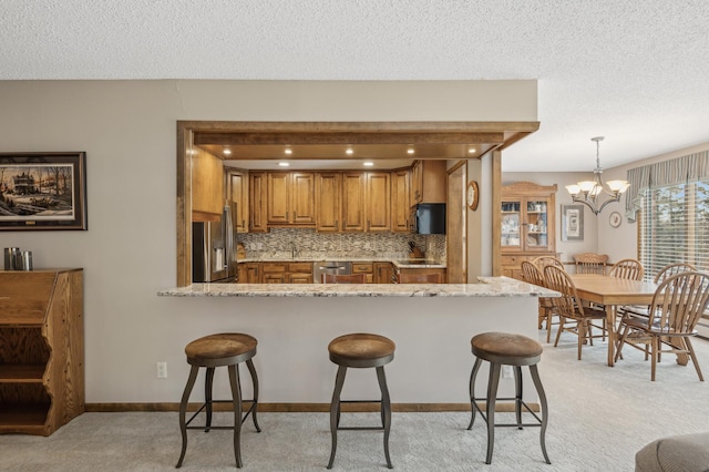 kitchen featuring appliances with stainless steel finishes, hanging light fixtures, light stone countertops, light carpet, and kitchen peninsula