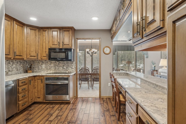 kitchen featuring appliances with stainless steel finishes, a notable chandelier, a textured ceiling, dark hardwood / wood-style flooring, and decorative backsplash