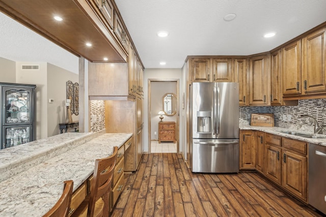 kitchen featuring stainless steel appliances, light stone countertops, sink, and backsplash