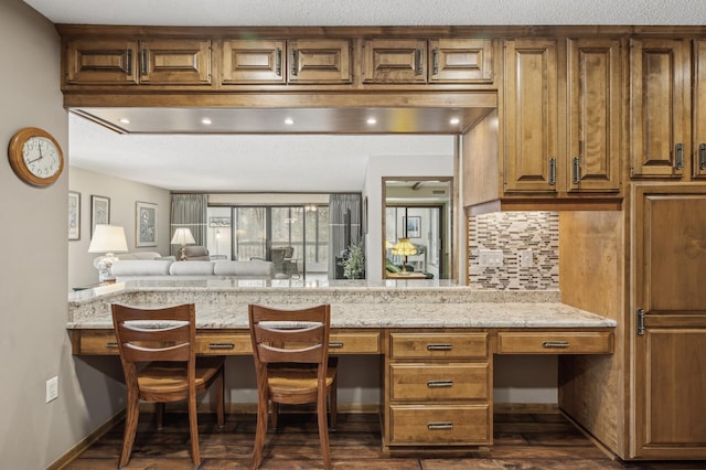 kitchen with built in desk, backsplash, light stone countertops, dark wood-type flooring, and a textured ceiling