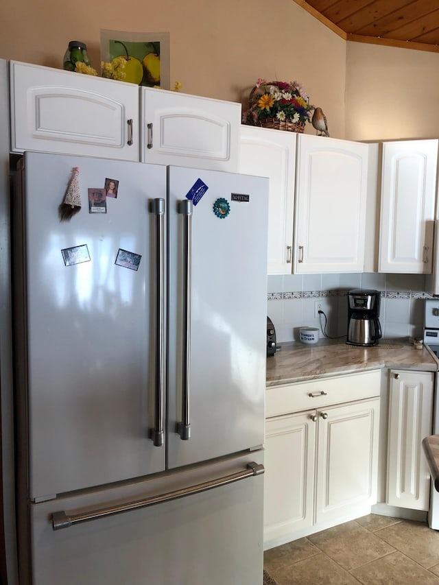 kitchen with high end fridge, decorative backsplash, white cabinets, and light tile patterned flooring