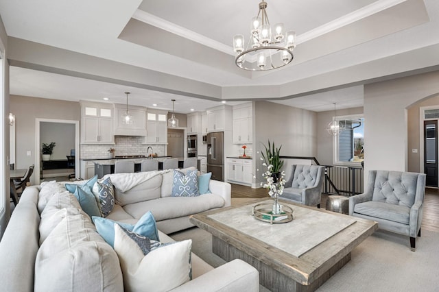 living room with a raised ceiling, crown molding, an inviting chandelier, and light hardwood / wood-style flooring