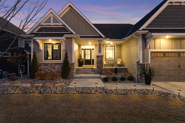 view of front of home with board and batten siding, stone siding, a porch, an attached garage, and a shingled roof