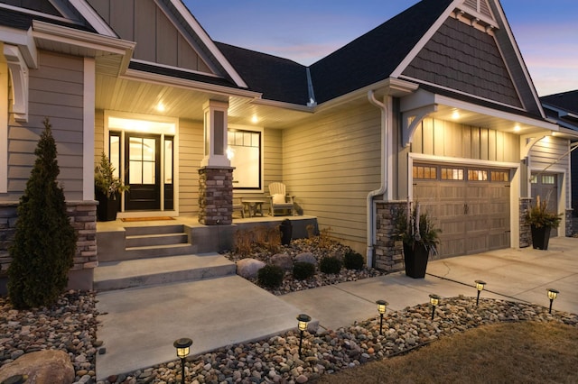 view of front facade with board and batten siding, a porch, concrete driveway, stone siding, and a garage