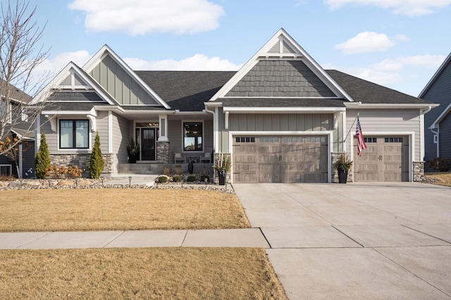 craftsman-style house featuring board and batten siding, an attached garage, concrete driveway, stone siding, and a front lawn