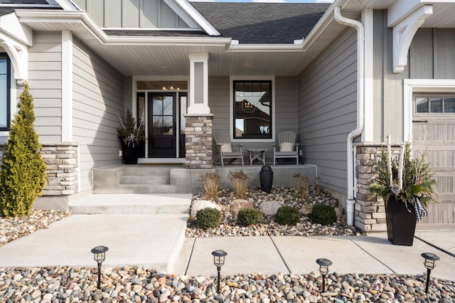 doorway to property with board and batten siding, covered porch, stone siding, and a shingled roof