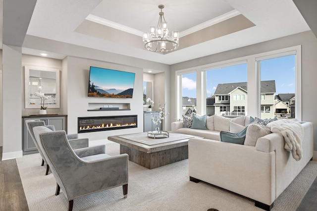 living room with a raised ceiling, a chandelier, a glass covered fireplace, ornamental molding, and wood finished floors