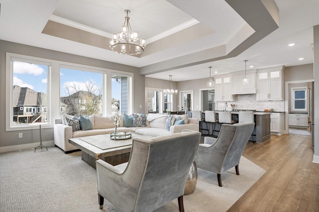living room featuring a chandelier, recessed lighting, a tray ceiling, light wood-style flooring, and baseboards