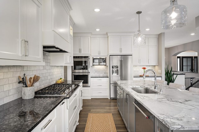 kitchen with a sink, appliances with stainless steel finishes, an island with sink, white cabinets, and dark wood-type flooring