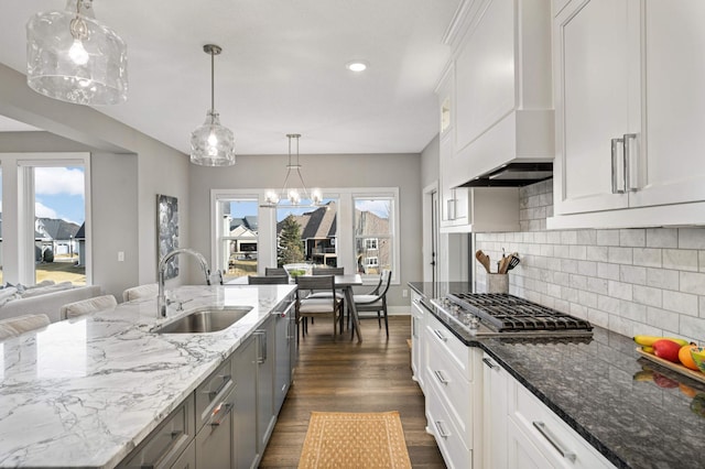 kitchen featuring a sink, stainless steel gas stovetop, dark wood-style flooring, backsplash, and light stone counters