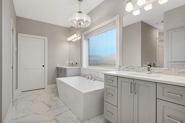 full bathroom with marble look tile flooring, decorative backsplash, a freestanding tub, baseboards, and a chandelier